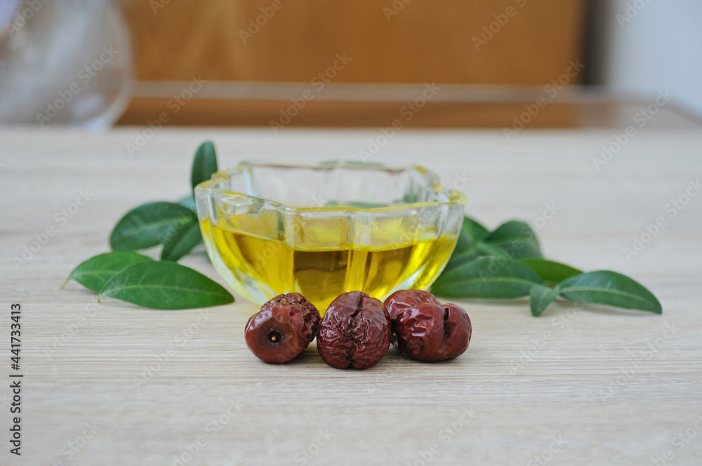 Jojoba fruits on the background of a cup with oil and green leaves. Selective focus on the anterior surface of the fruit. Jojoba fruits on the background of a cup with oil and green leaves. Selective focus on the anterior surface of the fruit.