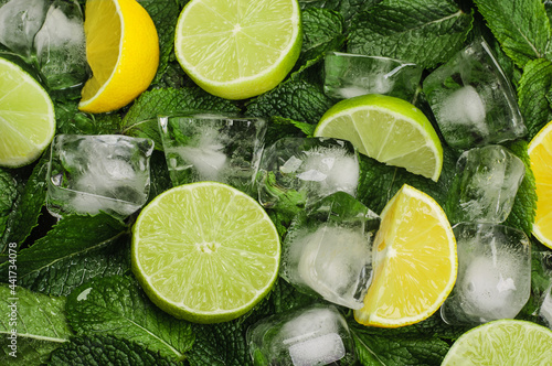 halves and wedges of limes and lemons with ice cubes on a background of fresh mint