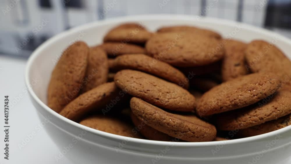 Rotating Of Fresh Brown Oatmeal Cookies With Sugar In A White Bowl On A White Kitchen Background. Rotating Of Fresh Brown Oatmeal Cookies With Sugar In A White Bowl On A White Kitchen Background.
