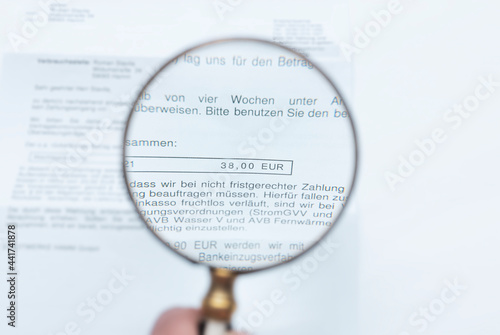 A man looks through a magnifying glass at an invoice.