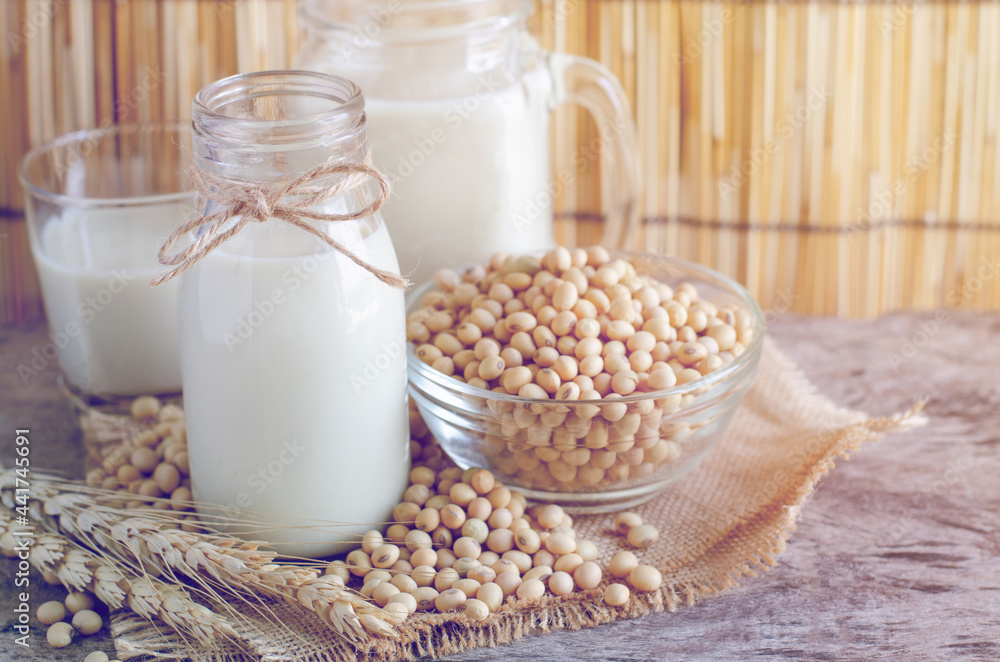 Closed up delicious homemade soybean milk in glass bottle with some seeds in glass bowl with dry wheat ear on wooden background in soft light vintage tone Closed up delicious homemade soybean milk in glass bottle with some seeds in glass bowl with dry wheat ear on wooden background in soft light vintage tone