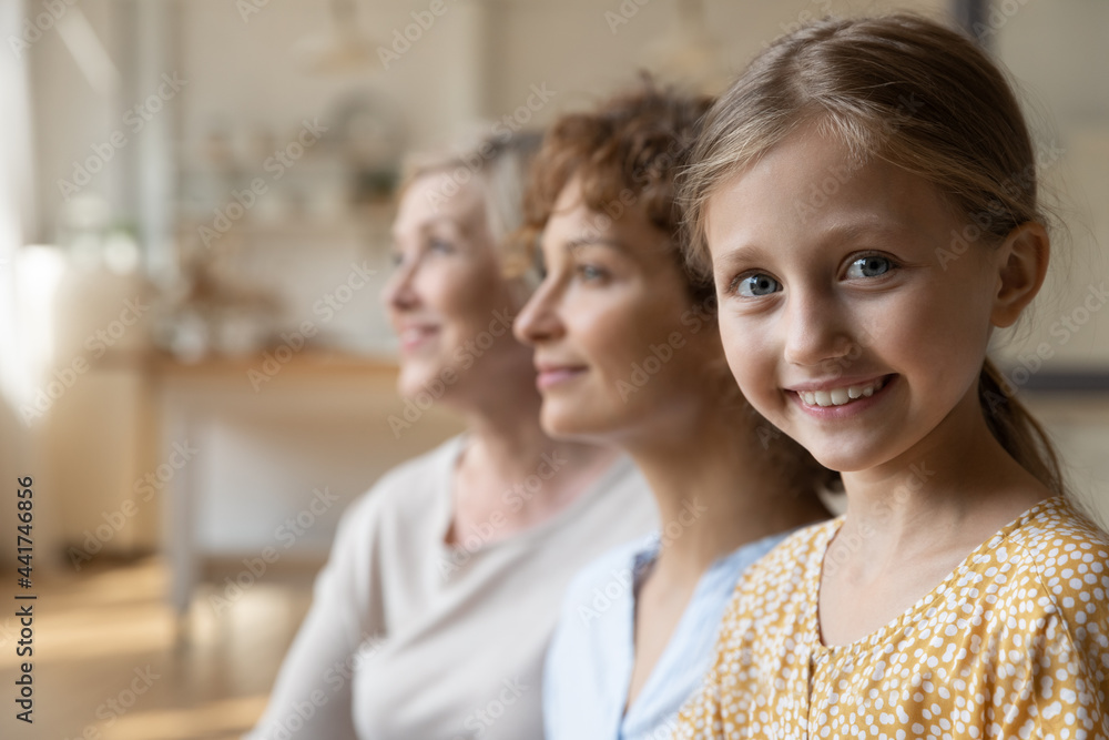 Head shot happy pretty cute emotional kid girl looking at camera, posing at home with dreamy blurred young mother and elderly granny, three female generations heredity, good relations concept. Head shot happy pretty cute emotional kid girl looking at camera, posing at home with dreamy blurred young mother and elderly granny, three female generations heredity, good relations concept.