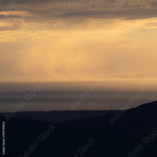 Lone wind turbine silhouetted against dramatic views of the Cumbrian Coastline. 
