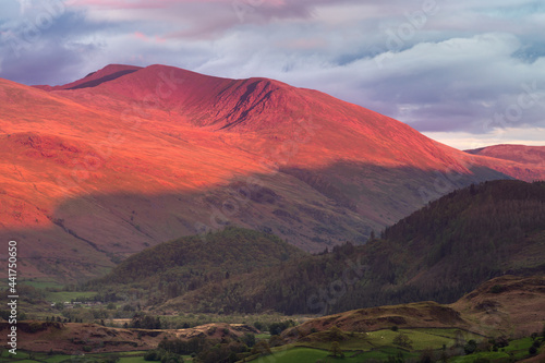 Evening light from the sunset casting a red glow and long shadows on Helvellyn mountain range in the English Lake District. 
