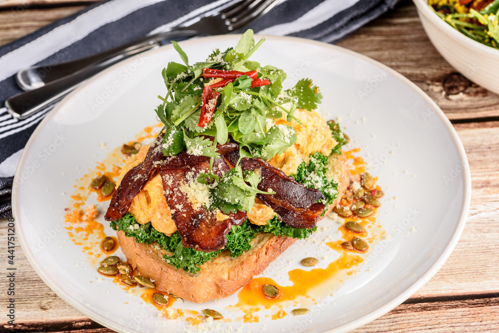 A serving of Chilli Scramble with smoked bacon, shallots, wilted kale and Asian herbs. Served on sourdough bread and shaved parmesan. A serving of Chilli Scramble with smoked bacon, shallots, wilted kale and Asian herbs. Served on sourdough bread and shaved parmesan.