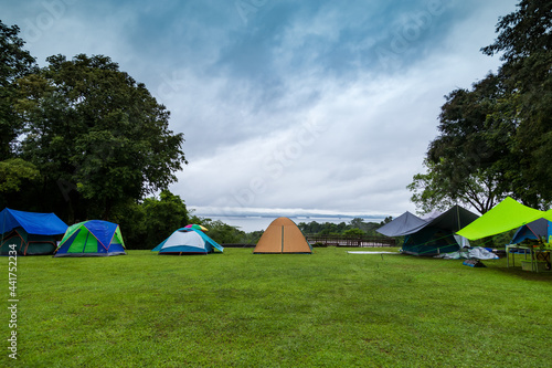 Many multi-colored tents spread out on the lawn and with trees, clear skies, suitable for relaxing.