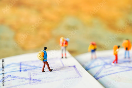 Miniature people: Group of traveler mini figures with backpack stand and walking on passport with stamps. Success Business Due around the world and Travelling agency concepts.