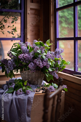 Bouquet of lilacs in a vintage basket. Beautiful violet Lilac flower still life Easter border design on wooden table.