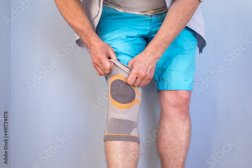 Man puts a special stabilizing brace on the injured knee joint. Studio, gray background. 