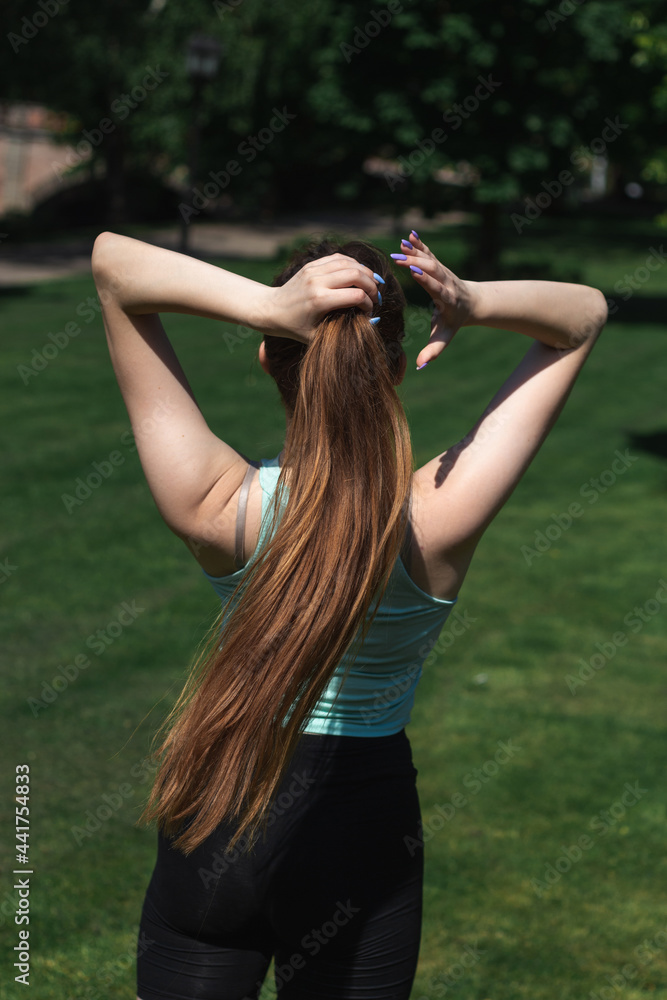 Young woman in sportswear is making a ponytail to start a workout outdoors Young woman in sportswear is making a ponytail to start a workout outdoors