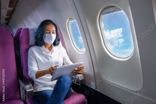 woman sitting on a plane sitting on a tablet and wear a mask to prevent coronavirus

