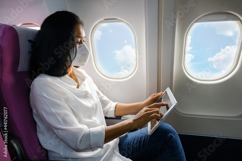 woman sitting on a plane sitting on a tablet and wear a mask to prevent coronavirus

