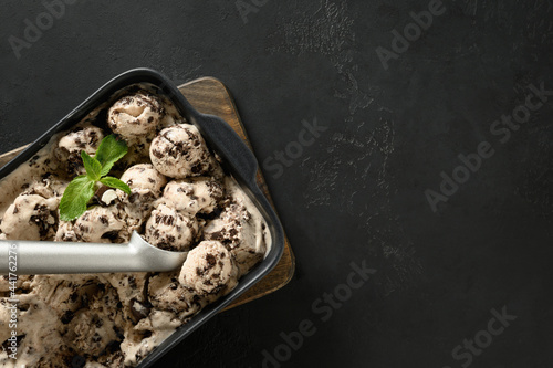 Homemade sugar free creamy ice cream with cookies in container on a black background with copy space. View from above. Tasty children dessert without sugar. photo