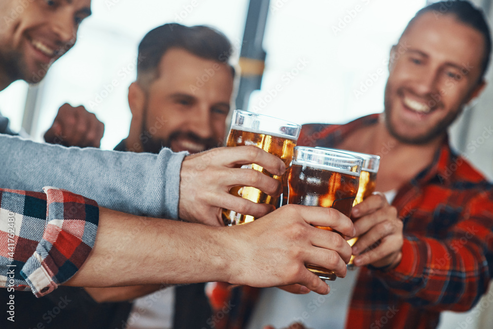 Happy young men in casual clothing toasting each other with beer and smiling