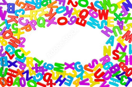 Background from multi colored plastic letters and numbers in a chaotic manner on a white backdrop. Place for text in the form of an oval. Copy space. English alphabet. Children school developmental co