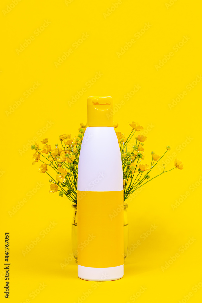 Organic cosmetic photo template for posters. Yellow decorative flowers in a glass and cream for face and hands on a yellow background Organic cosmetic photo template for posters. Yellow decorative flowers in a glass and cream for face and hands on a yellow background