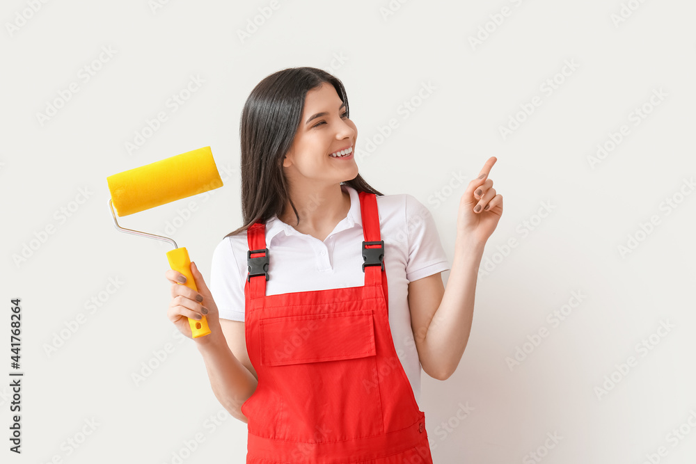 Young woman with paint roller pointing at something on white background