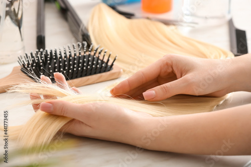 Female hairdresser with strand of blonde hair on table in beauty salon