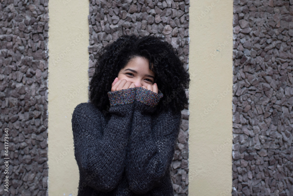 © ADDICTIVE STOCK - Ethnic woman in sweater covering mouth and looking at camera