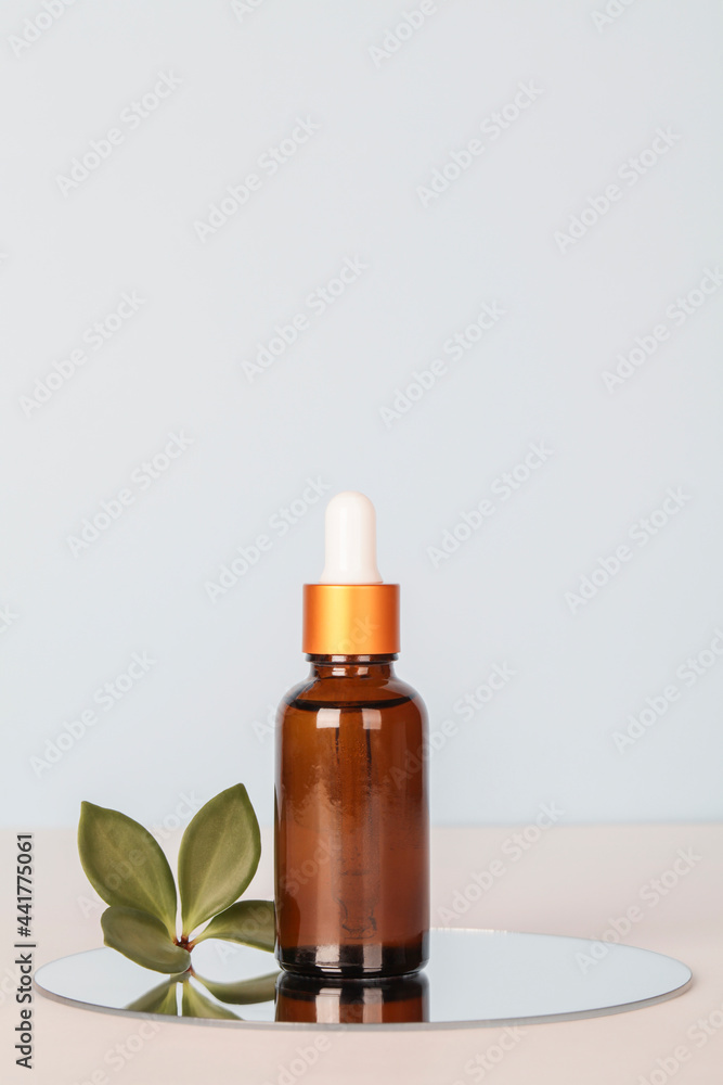 dark amber glass bottle with oil on mirror with green leaf on blue background. copy space. Beauty concept, brand packaging mock up.