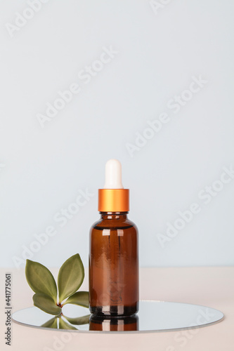 dark amber glass bottle with oil on mirror with green leaf on blue background. copy space. Beauty concept, brand packaging mock up.