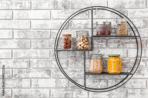 Jars with different products on shelf near brick wall