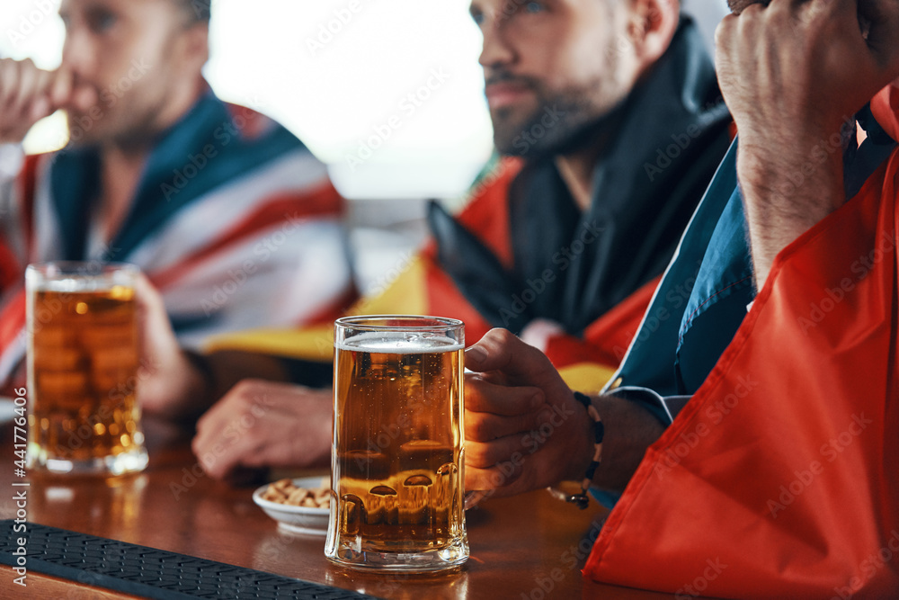 Close-up of young men covered in international flags enjoying beer
