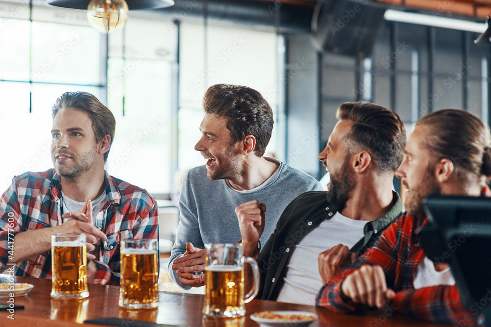Cheering young men in casual clothing enjoying beer while sitting in the pub Cheering young men in casual clothing enjoying beer while sitting in the pub