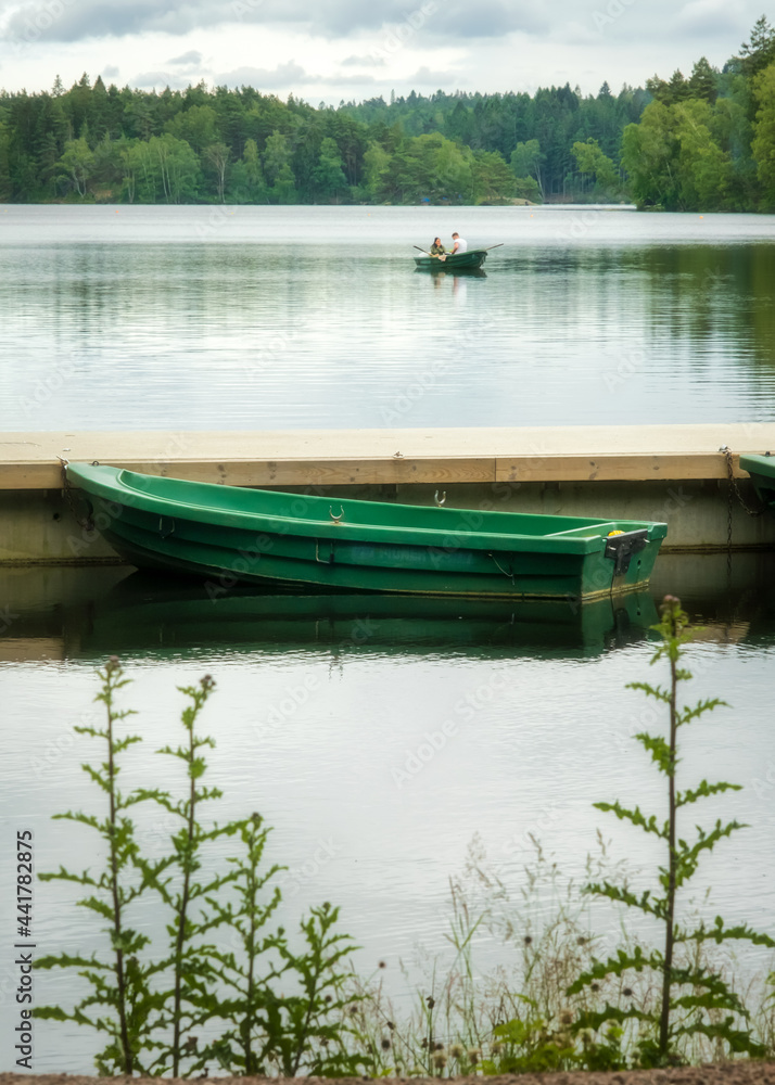 Green boat waiting for customer in the background young couple paddling canoe in swedish lake near gothenburg Green boat waiting for customer in the background young couple paddling canoe in swedish lake near gothenburg