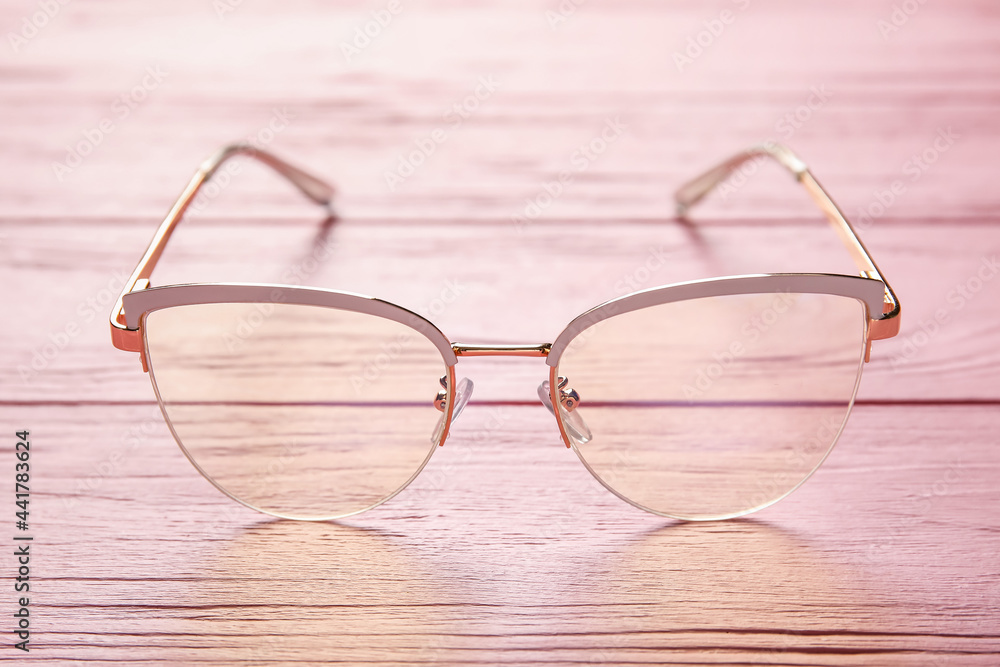 Stylish eyeglasses on color wooden background, closeup