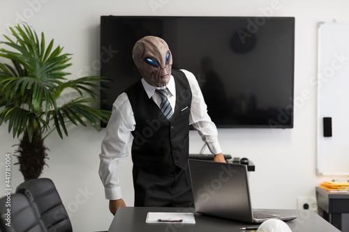 Quadro su tela A humanoid Alien in a white shirt, business suit looking at camera in the office with laptop