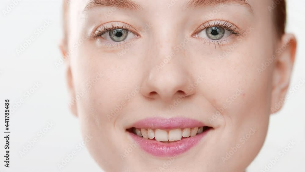 Extreme close-up shot of young Caucasian female skin care model massages her cheeks smiling wide for the camera on white background | Eye bags removal concept Extreme close-up shot of young Caucasian female skin care model massages her cheeks smiling wide for the camera on white background | Eye bags removal concept