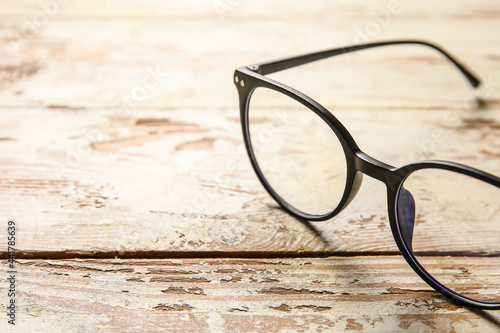 Stylish eyeglasses on light wooden background, closeup