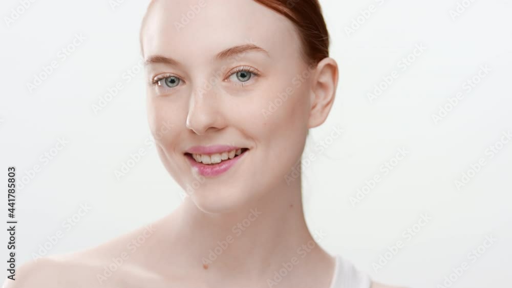 Beautiful Caucasian slim young woman with long red hair in ponytail touches her cheek smiling wide for the camera on white background | Skin moisturizing concept Beautiful Caucasian slim young woman with long red hair in ponytail touches her cheek smiling wide for the camera on white background | Skin moisturizing concept