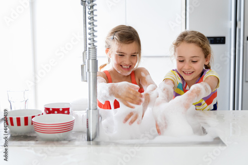 Happy sisters washing dishes in kitchen sink at home photo