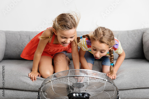 Two funny little girls on sofa facing a fan photo