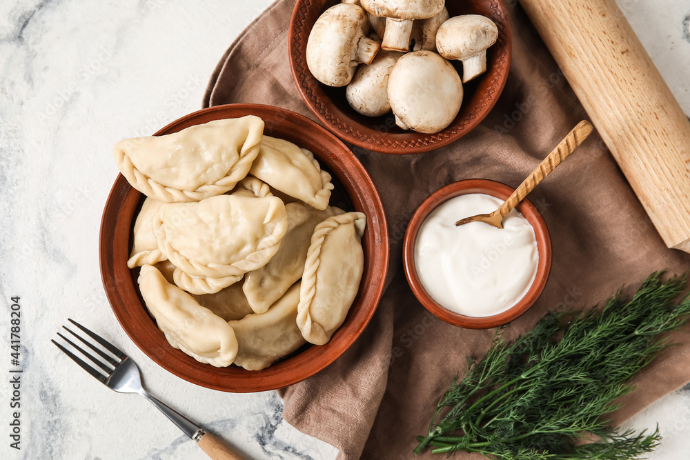 Bowl with tasty dumplings, sour cream and mushrooms on light background