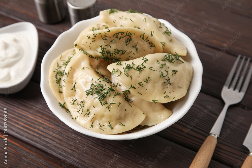 Plate with tasty dumplings and sour cream on dark wooden background Plate with tasty dumplings and sour cream on dark wooden background