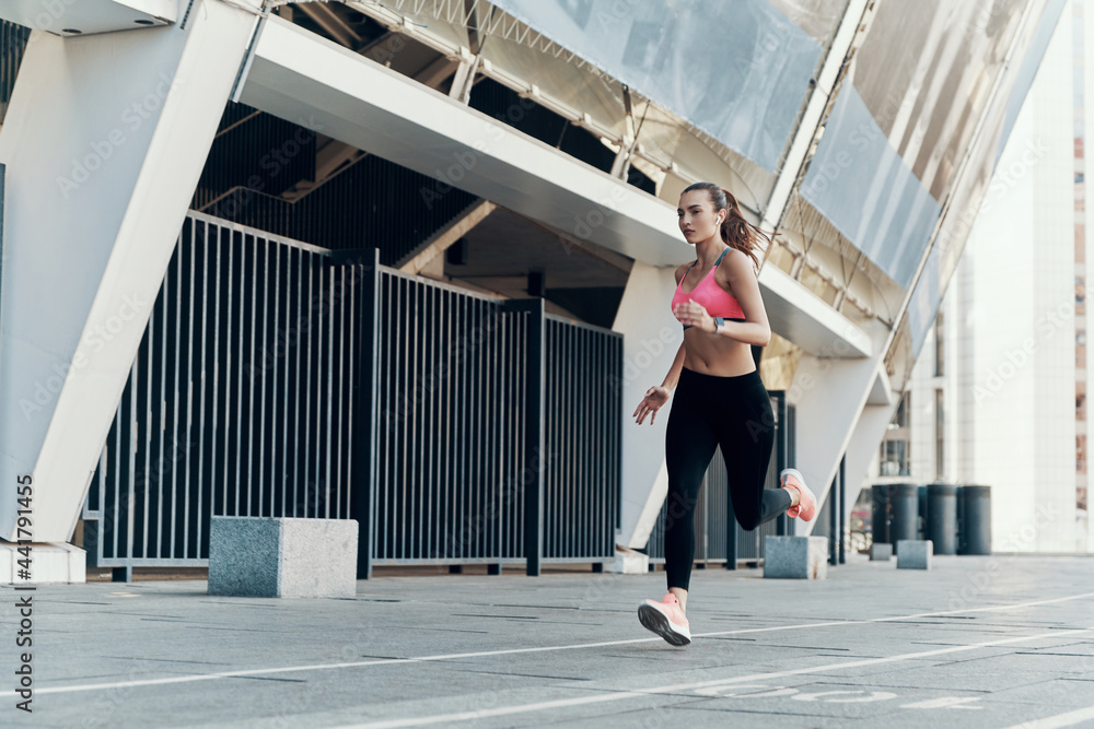 Full length of confident young woman in sportswear running outdoors Full length of confident young woman in sportswear running outdoors