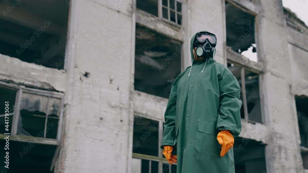 Man in protective clothing and a gas mask is standing on the background of ruined building. The concept of a post-apocalyptic world. Man in protective clothing and a gas mask is standing on the background of ruined building. The concept of a post-apocalyptic world.