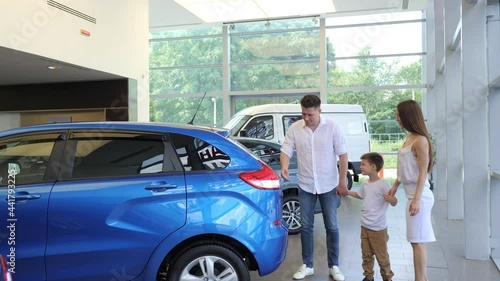 A beautiful couple with a young son is walking around the salon of a car dealership, looking at cars, picking up a vehicle for purchase. A family in a car dealership. Family purchase of a new car
