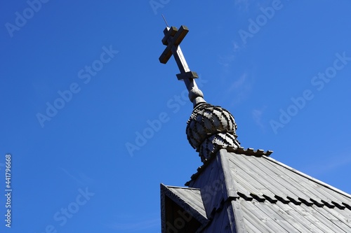 cross of a wooden church. Onion dome chapel. Orthodoxy. Roof tiles. Closeup view. blue summer sky. High quality photo