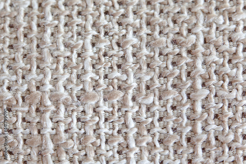 The texture of the fabric with a coarse weave of threads in natural beige tones, matting, close-up.