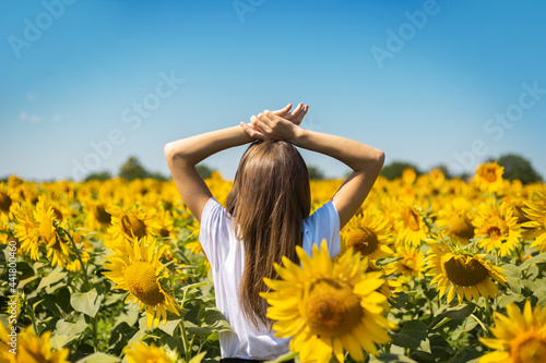 Young woman in white t-shirt with raised hands on a sunflower field on a summer sunny day