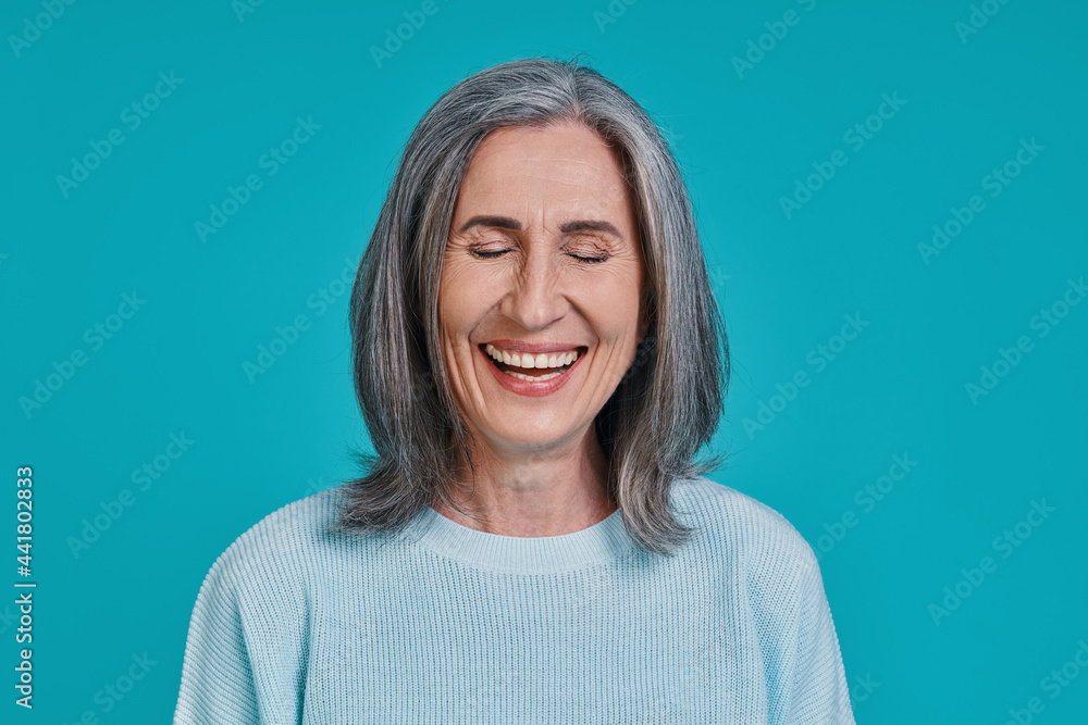 Headshot of mature beautiful woman laughing while standing against blue background Headshot of mature beautiful woman laughing while standing against blue background