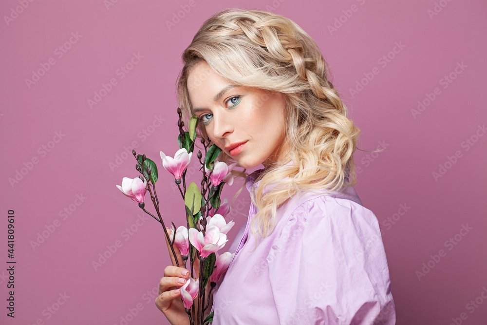 Attractive woman in pink dress holding flowers posing looking at camera on bright pink background, studio portrait
