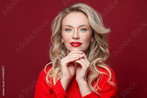 Smiling woman with blonde hair and natural manicured nails on vivid red background