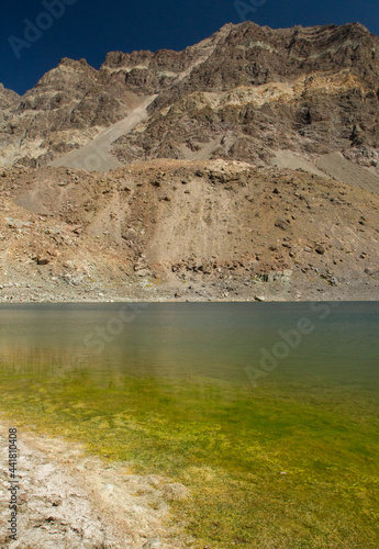 Natural background. View of the yellow shallows, blue water lake, rocky cliffs and mountains, high in the Andes cordillera in Chile.
