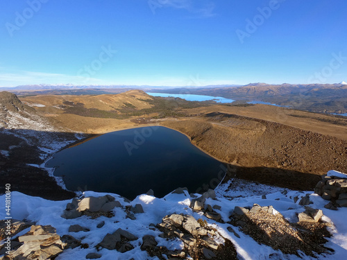 View of the deep blue water crater lake, forest, yellow meadow and Andes mountains, from the summit of volcano Batea Mahuida in Neuquén, Patagonia Argentina.  photo