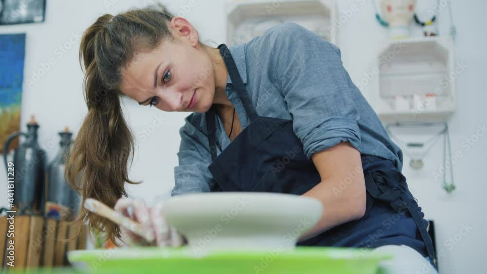 Female potter sitting and makes a cup on the pottery wheel. Female potter sitting and makes a cup on the pottery wheel.